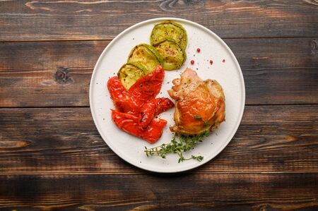 Homemade baked chicken thigh, zucchini and peppers with soy sauce, spices and herbs on a white plate on a wooden background. Copy space. Top viewの写真素材