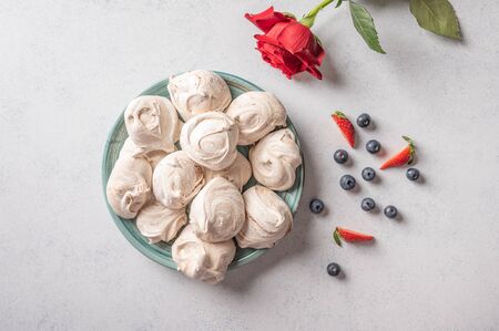 Homemade popular dessert meringue on a plate on white background. Nearby are strawberry and blueberry berries and red rose flowerの写真素材