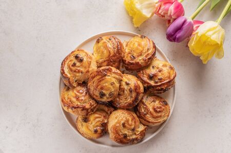 Homemade puff buns with custard cream and raisins in a ceramic plate on a light background. Nearby is a bouquet of colorful tulips. Top viewの写真素材