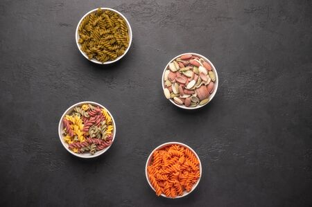 Various types of pasta on in multicolored bowls and scattered on classic dark rustic backgroun....