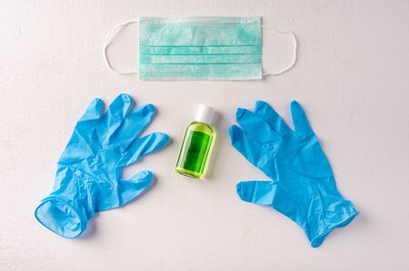 Hand sanitizer gel bottle, face mask, rubber gloves on light background. Copy space
