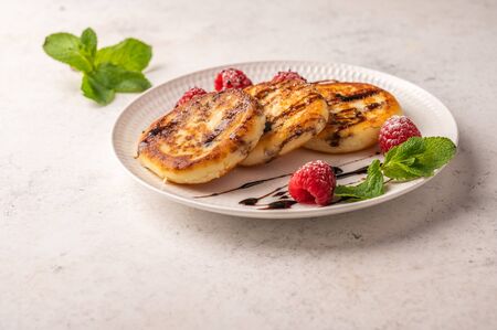Homemade cheesecakes with raspberries, syrup and mint on a ceramic plate on a light wooden...