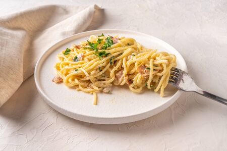 Classic homemade pasta carbonara Italian with bacon, eggs, parmesan cheese on light ceramic plate with fork and napkin on light table. Close up viewの写真素材