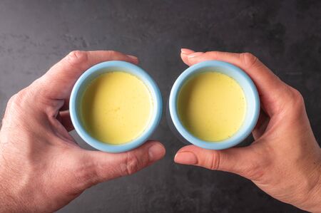Mens and womens hands are hold side by side blue ceramic cups with traditional Indian masala chai tea. Close up top view selective focusの写真素材