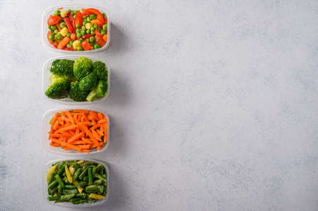 Frozen vegetables mix carrot, broccoli, spinach, green pods beans in plastic trays on light...