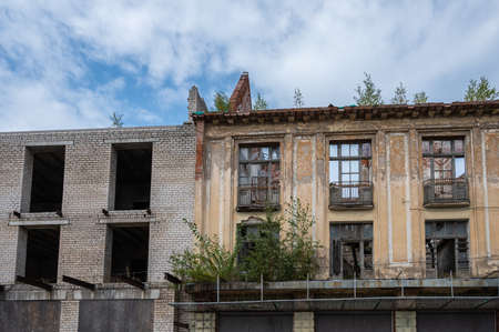 Facade of the old destroyed building with a brick extension against a blue sky with clouds, copy space, horizontal viewの写真素材