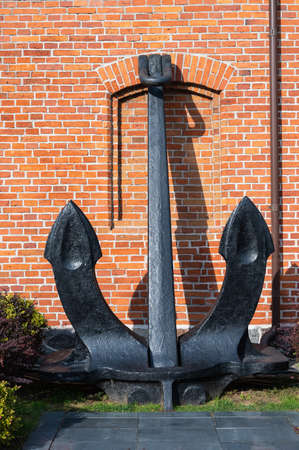 Large ship anchor against a red brick wall on a sunny day, vertical orientation