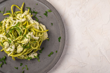 Close up pasta with pesto, stracciatella cheese and parsley served on gray ceramic plate on light background, selective focus, top view, copy spaceの写真素材