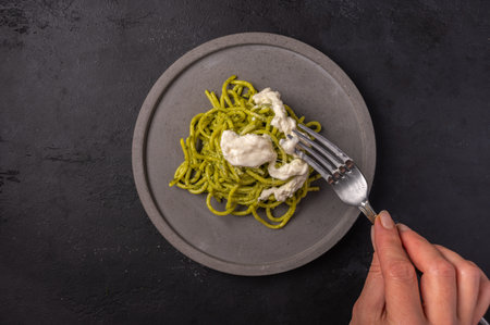 Womans hand holds a fork with a paste with strachatella and pesto, selective focus, top viewの写真素材