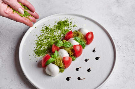 Womans hands sprinkled with green breadcrumbs to delicious italian caprese salad with ripe tomatoes, fresh garden basil and mozzarella cheese. Close up, food styleの写真素材