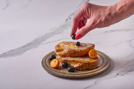 Womans hand puts a blueberry on homemade traditional Spanish torrijas or French toasts. Popular dessert for Christmas, Easter or Pascua. Top viewの写真素材