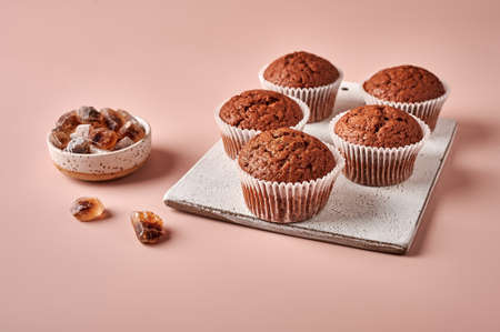 Homemade chocolate cupcakes in baking paper forms on cutting board on pink powdery background, selective focusの写真素材
