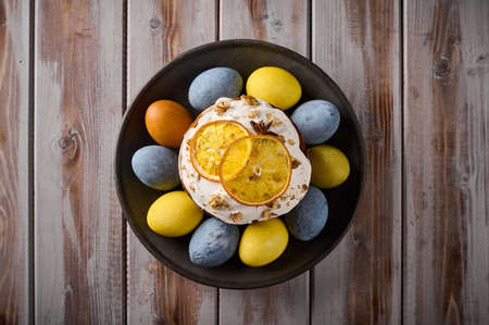 Homemade Easter cake and multi-colored painted eggs on black platter against a background of textured boards. Top view, copy spaceの写真素材
