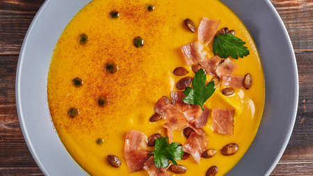 Panoramic view traditional pumpkin puree cream soup with carrots, onions, ginger, garlic, coconut milk. Added seeds, fried bacon, parsley. Healthy, vegetarian foodの写真素材