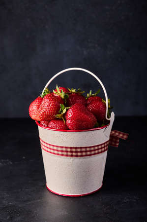 Strawberry in light bucket on black background, vertical orientation, copy spaceの写真素材