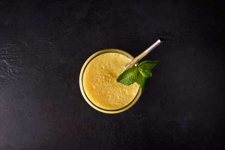 Top view mango lassi in glass with tube on dark background. Traditional Indian and Pakistan drink