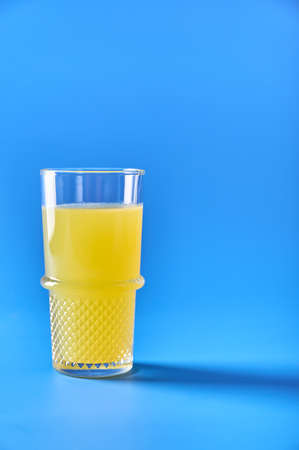 Orange juice in glass on blue background. Refreshing summer drink. Copy space for your text. Vertical orientationの写真素材