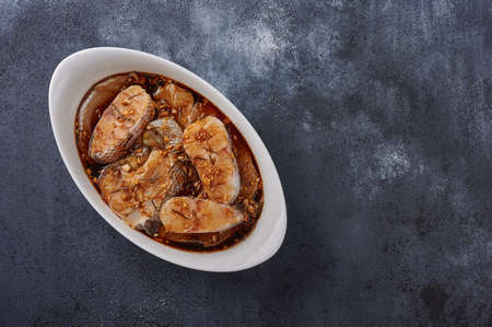 Baked white sea fish macrourus in marinade of olive oil, rosemary, spices in white pan on dark textured background. Top view, copy spaceの写真素材