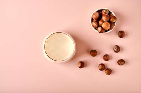 Hazelnut milk in glass and nut seeds on pink powder background. Top view. Copy spaceの写真素材