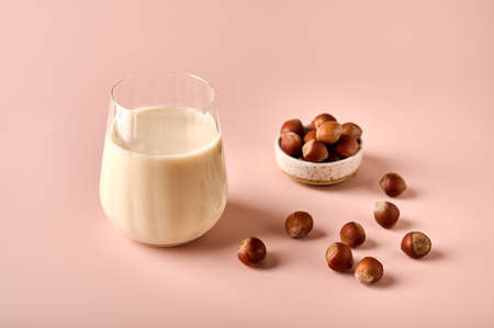 Hazelnut milk in glass and nut seeds selective focus on pink powder background. Close upの写真素材