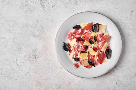 Prosciutto coppa di parma ham slices with parmesan cheese and dark basil on light plate on textured background. Top view with copy spaceの写真素材