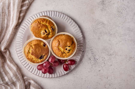 Flat lay homemade cupcakes with cherries and grapes on plate with napkin on light background, copy spaceの写真素材