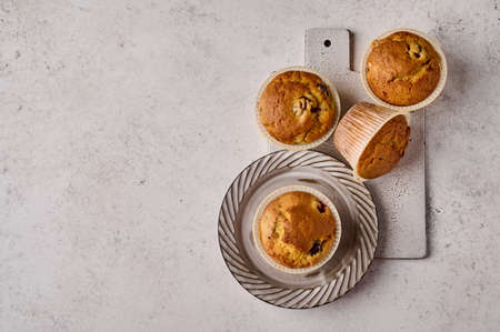 Top view cupcakes in baking paper forms on plate and scratched ceramic cutting board on gray...