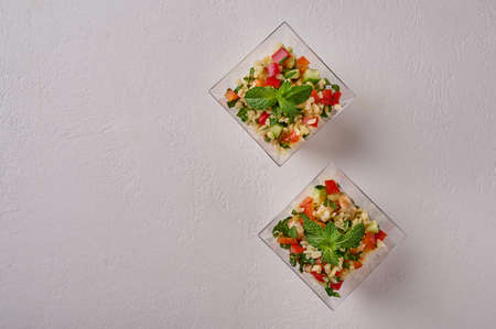 Tabbouleh salad flat lay. Traditional Middle Eastern dish with parsley, mint, bulgur, tomatoes in transparent buffet shape cup on white background. Copy spaceの写真素材