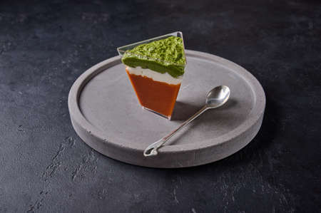 Verrines from baked pepper with creamy gorgonzola and pesto in transparent buffet shape cup on grey ceramic plate with spoonの写真素材