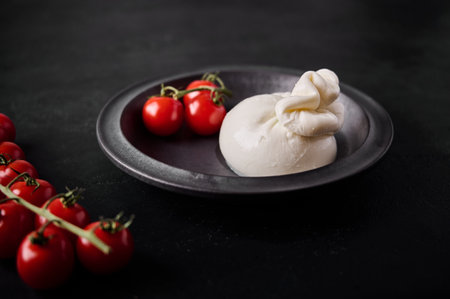 Italian burrata cheese and branch of cherry tomatoes on dark plate. Selective focus. close up. Low keyの写真素材