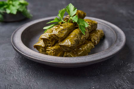 Delicious stuffed grape leaves, traditional Middle Eastern dish dolma or sarma, with parsley in black plate on dark wood background. Close upの写真素材