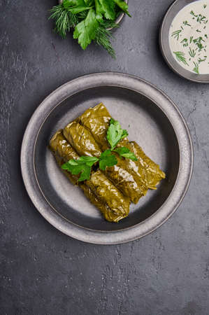 Vertical orientation dolma, parsley, saucepan with sour cream on ceramic color graphite plate on dark tableの写真素材