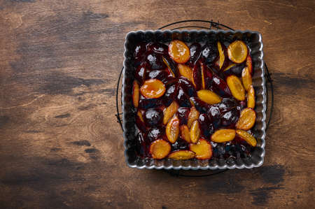 Caramelized in sugar syrup pieces of plums in baking dish on wooden table, top view, copy spaceの写真素材