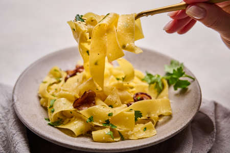 Womans hand holds a fork with Italian pasta pappardelle with mushrooms chanterelles, cheese and parsley. Macro, selective focusの写真素材