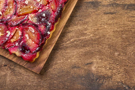 Tart or pie with plums on a wooden cutting board on rustic background. Top view, copy spaceの写真素材