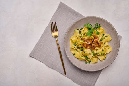 Italian pasta pappardelle with mushrooms chanterelles, cheese and parsley on plate with golden fork and napkin, top viewの写真素材
