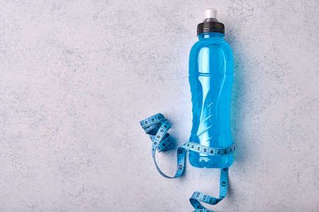 Isotonic energy blue transparent sport drink in plastic bottle and measure tape on grey textured background. Allows to maintain the most optimal balance of water, salt and electrolytesの写真素材
