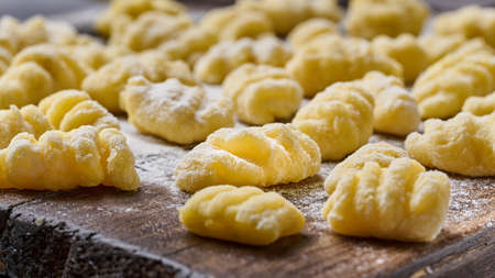 Homemade raw uncooked potato gnocchi with flour and grated parmesan cheese over wooden cutting board. Macro, selective focusの写真素材
