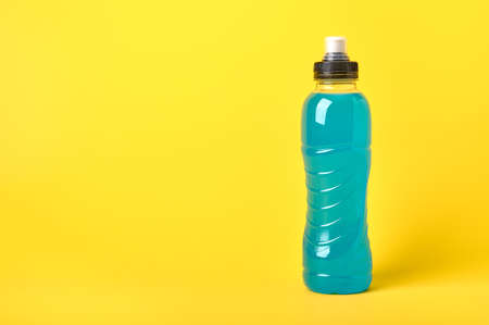 Isotonic energy blue transparent sport drink in plastic bottle on yellow background. Allows to...