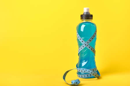 Isotonic energy blue transparent sport drink in plastic bottle and measure tape around it on yellow...