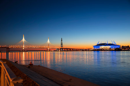 Stadium "Saint Petersburg Arena" on Krestovsky island, cable-stayed bridge western high-speed diameter across Peter's fairway and fishermen on the waterfront  in St. Petersburg at sunset, Russiaのeditorial素材