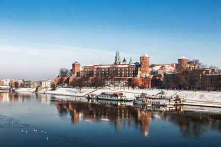 Ancient Royal Wawel castle on the banks of the Vistula river with tourist boats at the pier in...