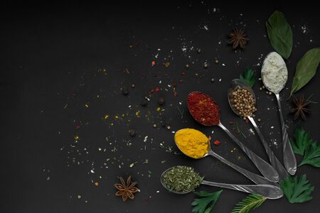 Set of various spices and herbs on black slate background.