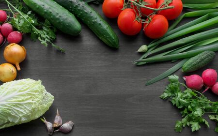 Summer ripe vegetables on the table. Cooking in the kitchen. Tomatoes, cucumbers, salad, onions, parsley, radishes, garlic, spices. Ingredients for the dish. Tasty and healthy. Vitamin salad. Diet food. Black background Empty space frameの写真素材
