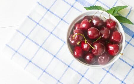 Fresh ripe cherry on a white ceramic plate on a napkin on a wooden white background. The concept of Healthy food and tasty dessert. Diet vegetarian. Close up. Copy spaceの写真素材
