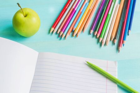 Concept back to school.School accessories, colored pencils, pen, apple with empty notebook on blue wooden background. First of September. drawing. Autumn. Studying at the College. Close up. copy spaceの写真素材