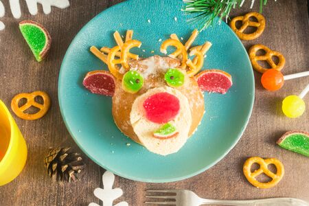 Christmas edible deer of buns and marmalade on a plate on a wooden table next to candy and Christmas tree branches.Kids food.Christmas edible food..Christmas minimalism.の写真素材