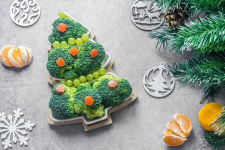 Creative edible Christmas tree of fresh broccoli next to Christmas tree and tangerines.Concept: vegan holiday ideas.Healthy food.New year food background.top view.Holiday,celebration, food art conceptの写真素材