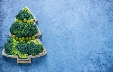Creative edible Christmas tree of fresh broccolion on a blue background.Vegan holiday ideas.Healthy food.New year food background.Holiday,celebration, food art concept.Minimalism.Top view.Copy spaceの写真素材