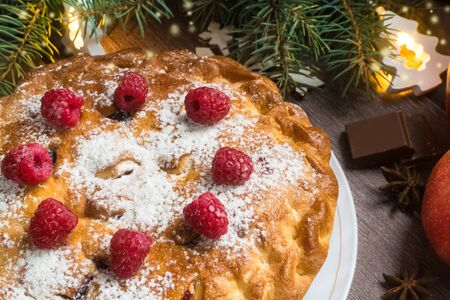 Delicious raspberry pie with berry jam, icing sugar and spices for Thanksgiving or Christmas on dark background.Christmas lights.Apples, chocolate, garlands.Festive dinner.Christmas eve.Party.Close upの写真素材
